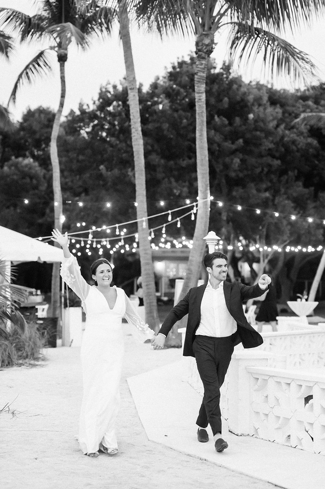 bride and groom holding hands and entering their Islamorada wedding reception while cheering along with their wedding guests captured by Florida Keys photographer