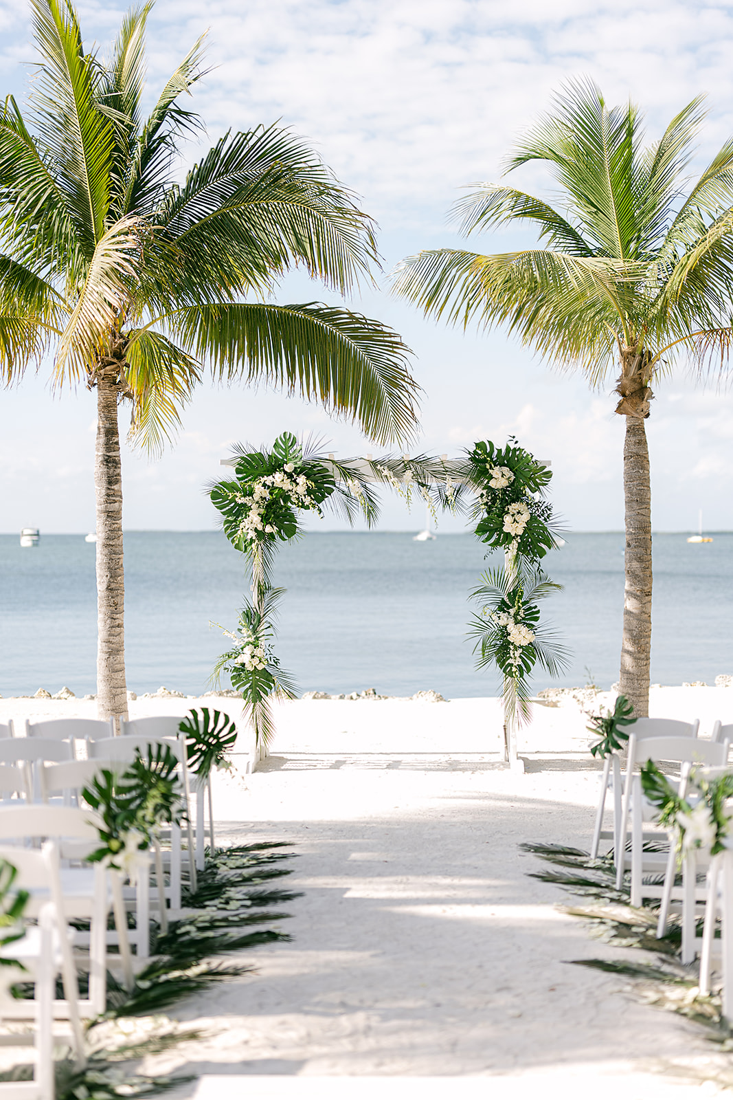 beach wedding ceremony set up in Key Largo with white folding chairs, palm trees and floral arrangements made of palm leaves and white florals